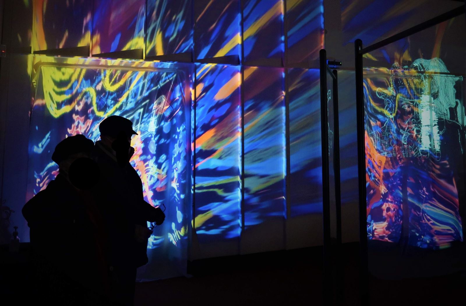 The shadows of two people in front of a very colourful projection